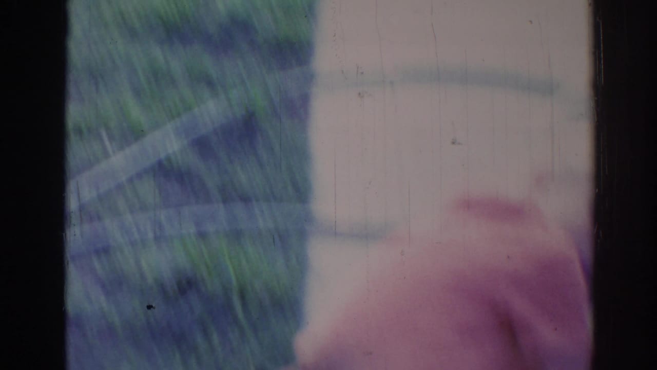Blurred greenery and part of a light exterior seen through aged 8mm film.