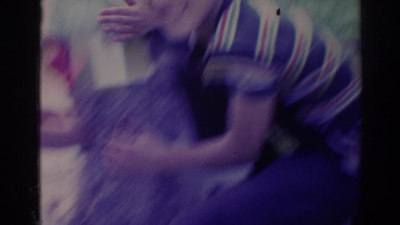 Blurred person in a patterned top near another figure in low blue-purple light.