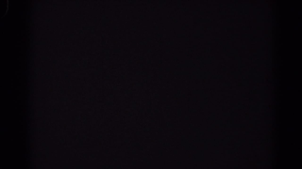 Dark, underexposed 8mm frame with faint scratches and no identifiable parade detail visible.