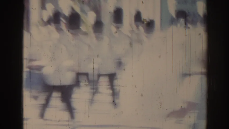 Blurred 1967 Los Angeles 8mm frame showing light-uniformed parade participants or musicians moving through a street-like setting.