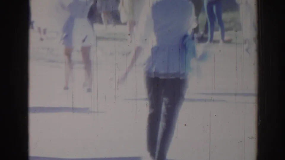 1967 Los Angeles 8mm frame showing a blurred pedestrian near a parade route in strong sunlight, with visible film wear.