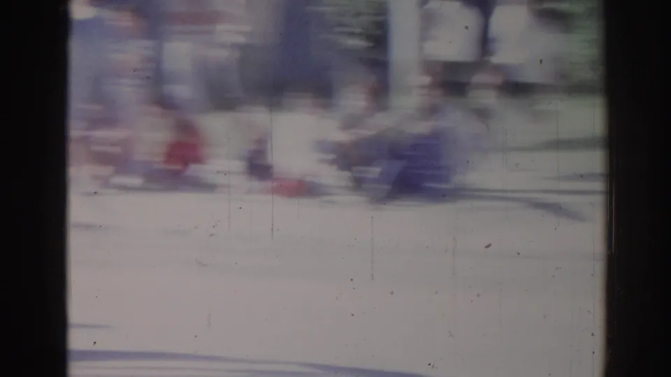 1967 Los Angeles 8mm frame showing blurred pedestrians and street movement near the parade route, with blue-white color cast.