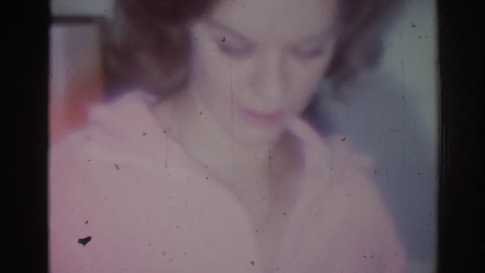 Blurred close-up of the woman looking down, with film grain and soft color in the 1967 home-movie frame.