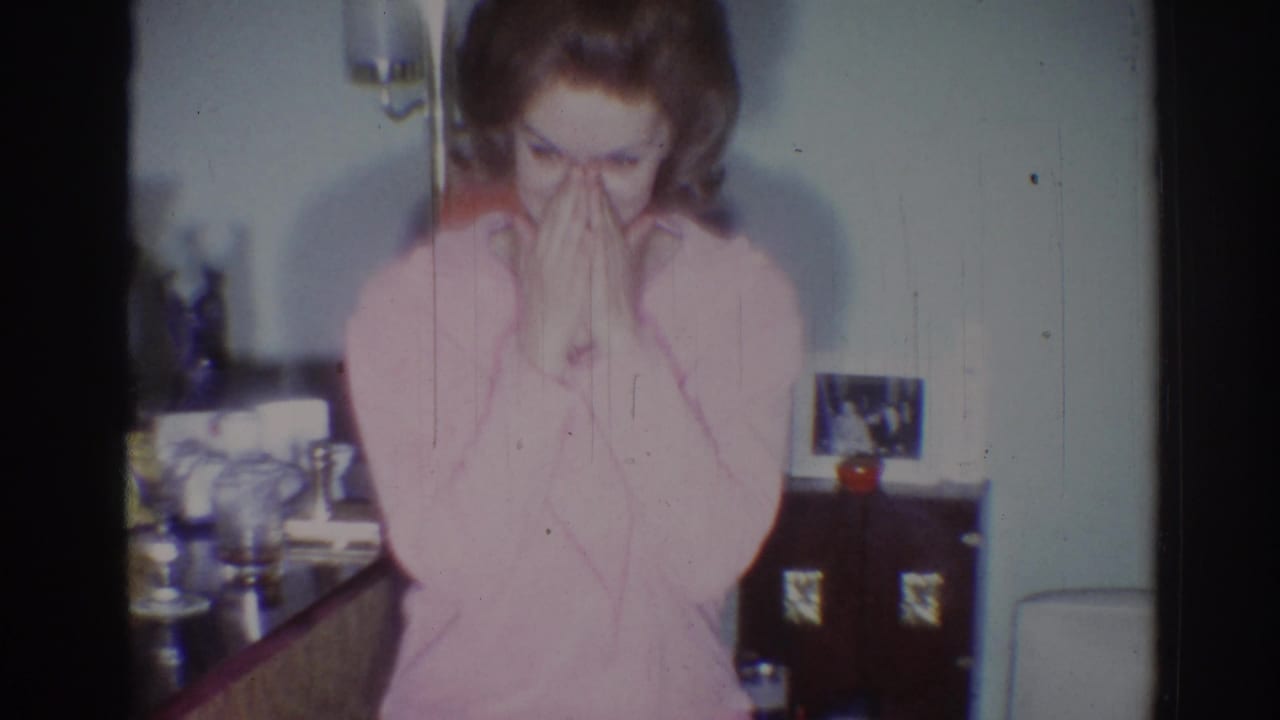 Adult woman in a pink sweater covers her mouth while standing or sitting indoors.