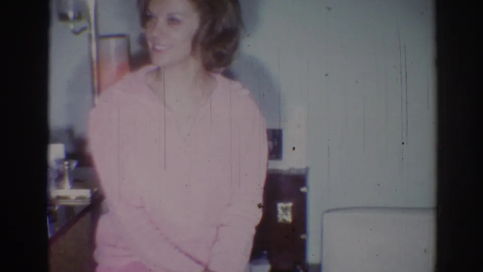 Young woman in a pink sweater turns slightly while smiling in 1967 Los Angeles home-movie footage.