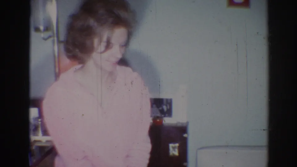 Young woman with styled hair looks down in a private Los Angeles interior, captured on 8mm film in 1967.