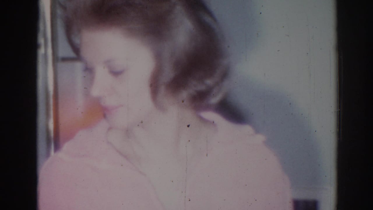 Soft-focus woman in a pink top looking downward inside a dim home interior.