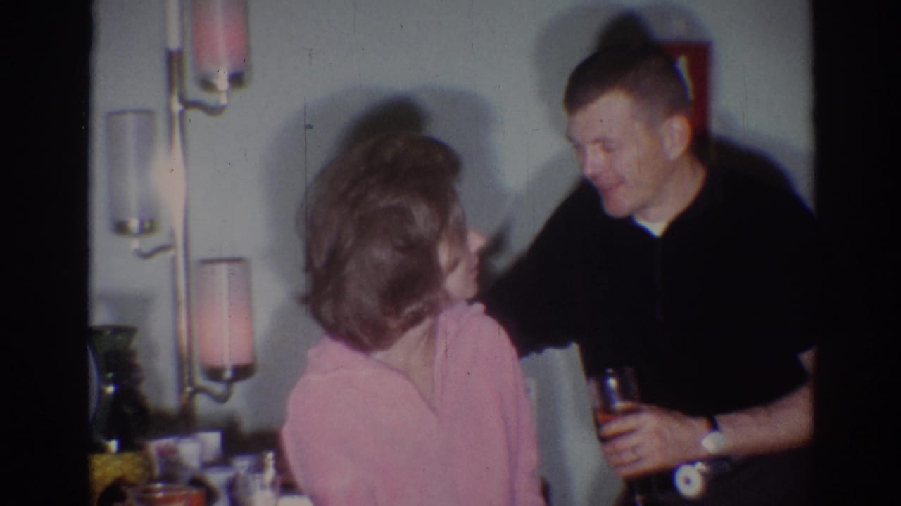 1967 Los Angeles home-movie frame with a woman in a pink top and bouffant hairstyle facing a man holding a drink indoors.