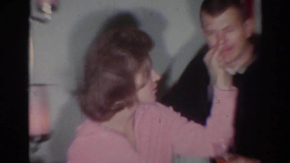 1967 Los Angeles party frame showing a woman reaching toward a man's face in a playful, blurred home-movie moment.