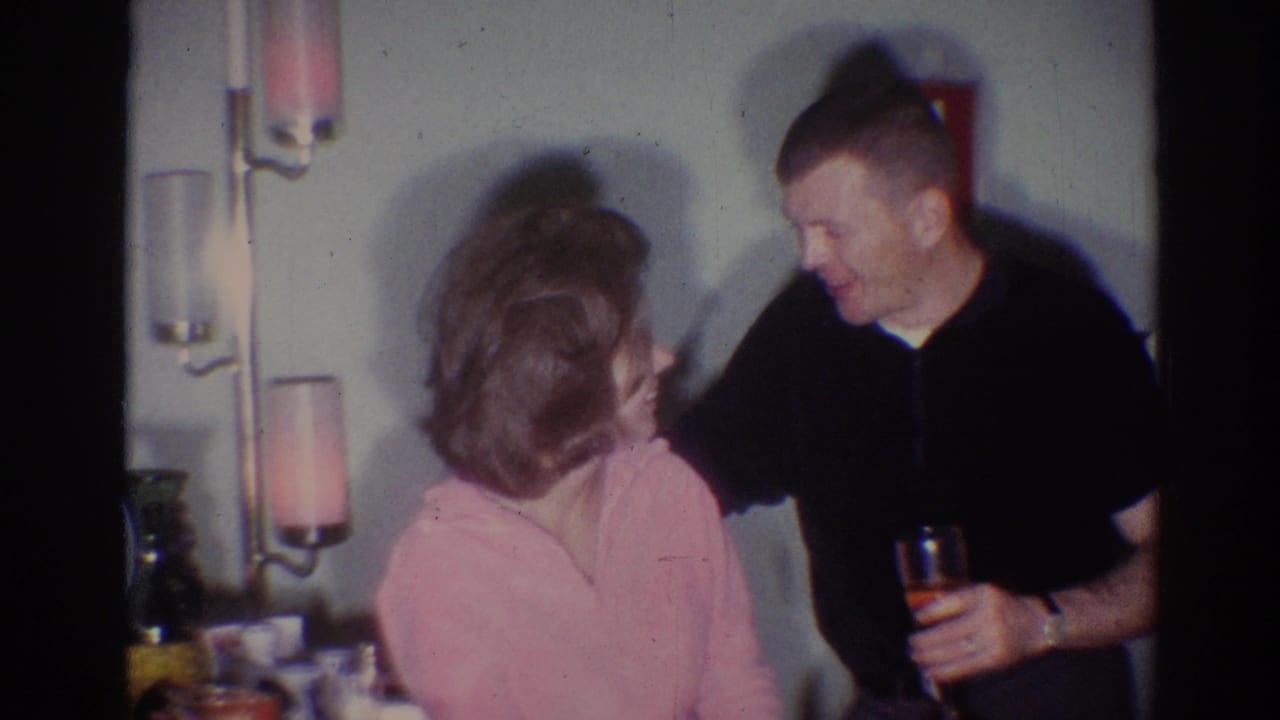Man in a black shirt leans toward a seated woman in a pink top at an indoor party.