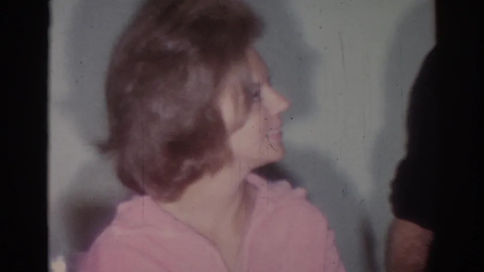 Close 1967 Los Angeles home-movie frame of the woman in a pink robe looking right toward the man at the edge of the frame.