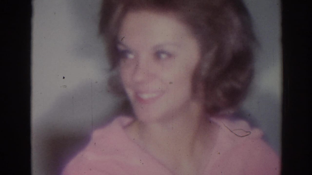 Woman in a pink top smiling in a softly focused interior close-up.