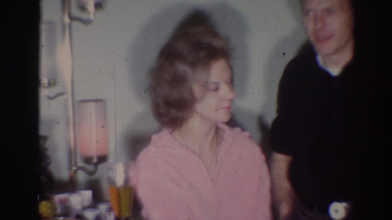 In a 1967 Los Angeles home interior, a seated woman in pink looks toward a standing man in a dark shirt.