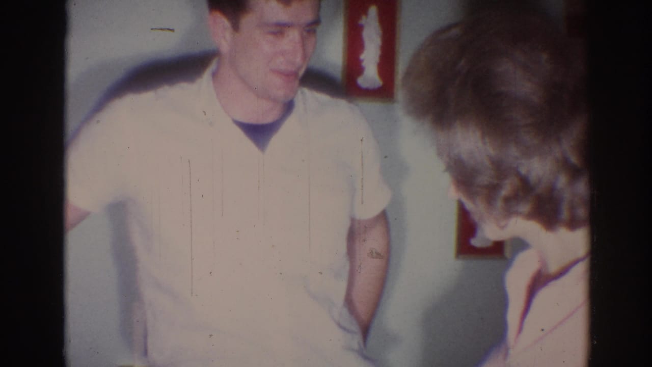 Man in a light short-sleeve shirt smiles beside a woman inside a home.