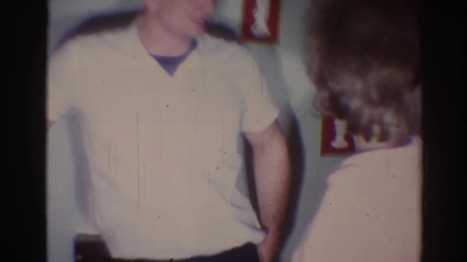 A man in a pale shirt stands with his arm behind his back while a woman turns toward him in a 1967 Los Angeles interior.