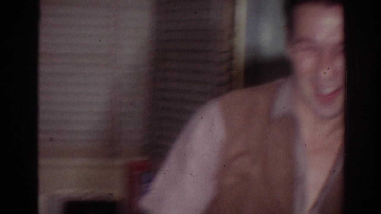 Blurred man moving in a dim room with blinds behind him.
