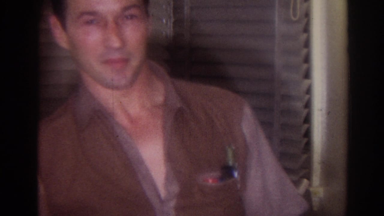 Man in a brown vest looks toward the camera inside a dim room.