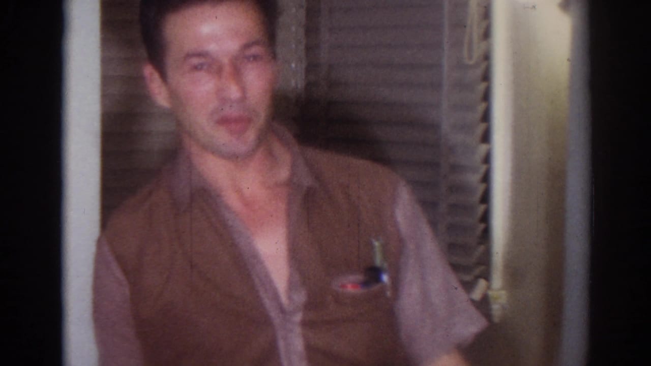 The man in the brown vest remains framed near shutters, appearing to speak or react to the camera inside a Los Angeles home.