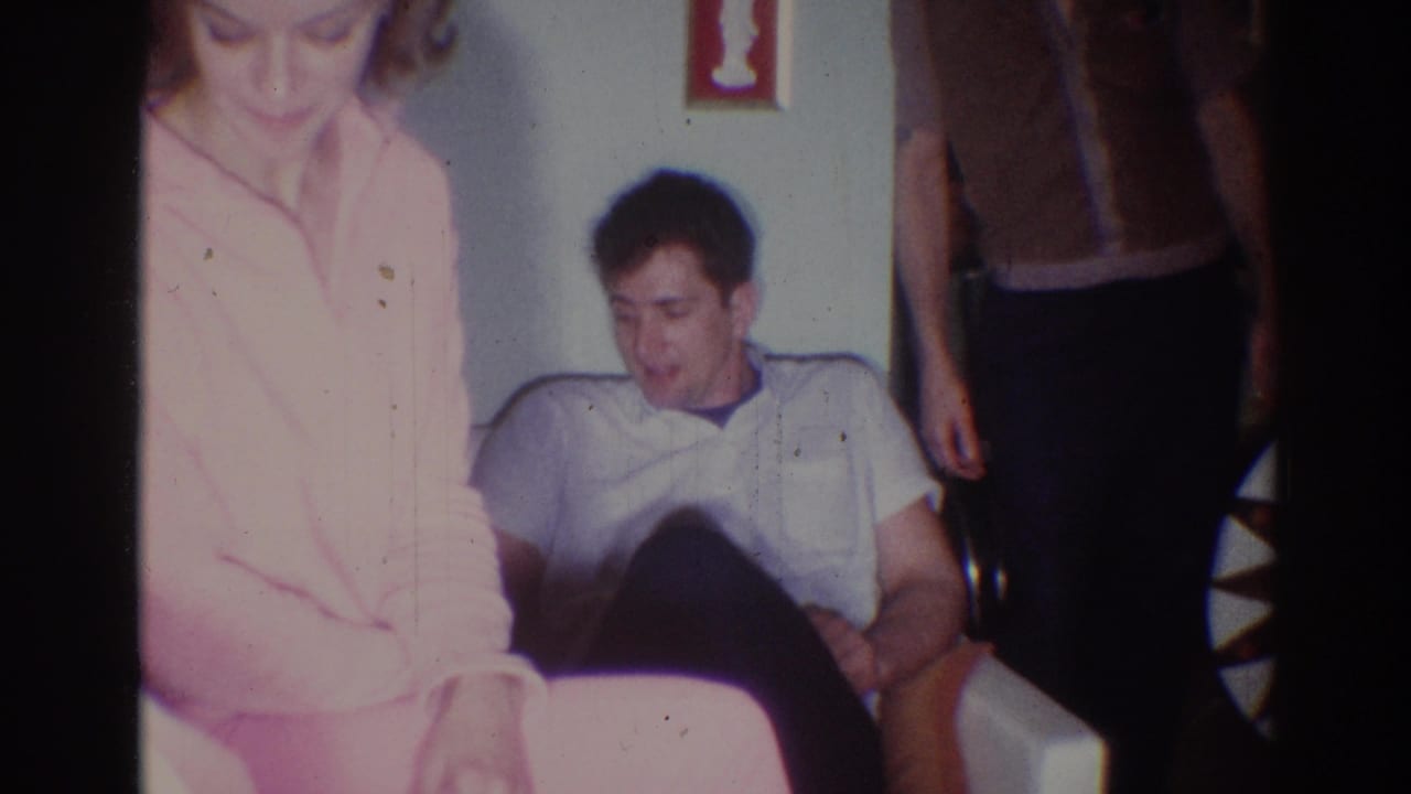 Young man seated on a white couch while a woman in pink leans nearby.