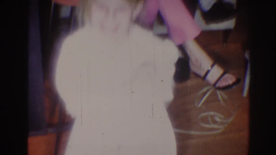 1967 Los Angeles living-room frame with a bright foreground figure, a chair, wood floor, and adults partly visible at the edges.