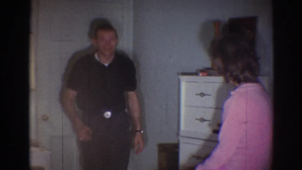 A man in a dark shirt faces a woman in pink beside a white dresser, captured with soft 8mm focus in a 1967 Los Angeles home movie.