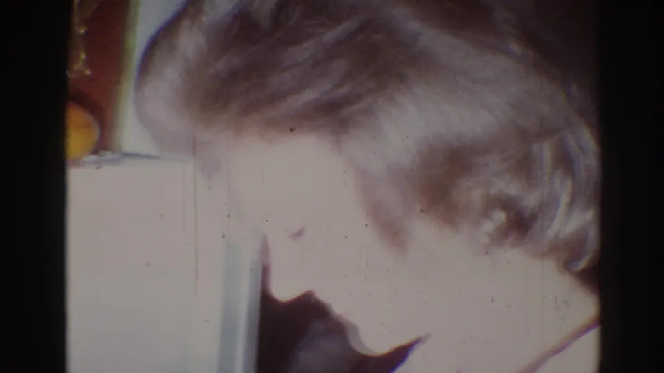 The final frame shifts close to a blond-haired person leaning down near pale furniture, with the interior details softened by 8mm exposure.