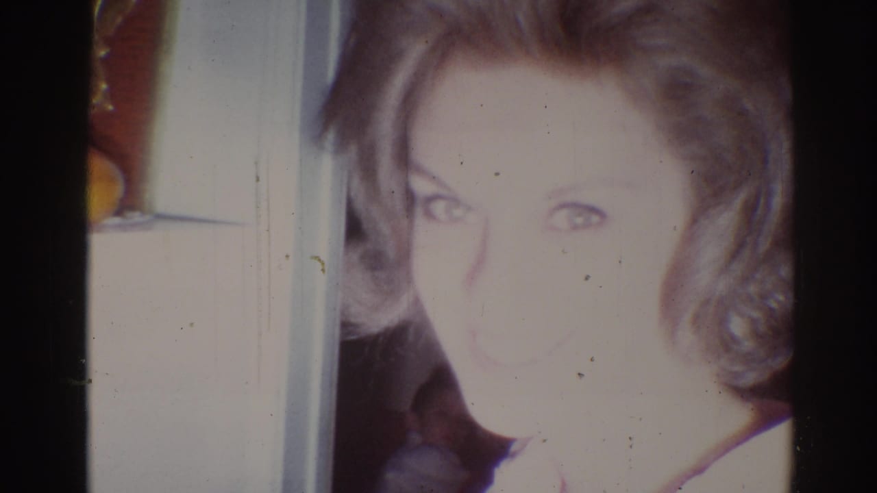 Blonde woman smiling toward the camera inside a softly lit room.