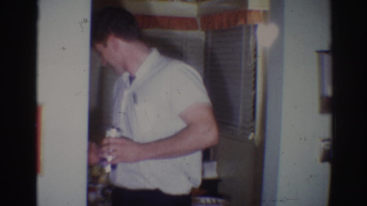 Man in a white short-sleeved shirt holds a can near a doorway inside a home.