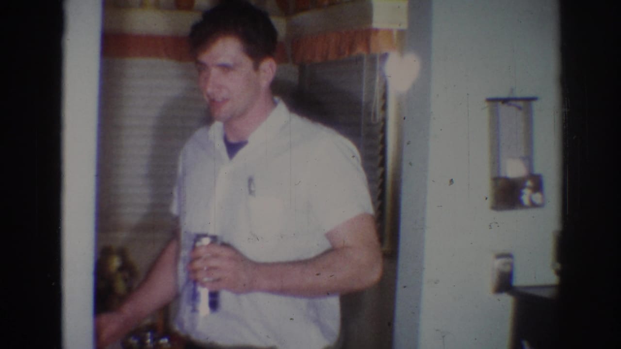 Man faces partly toward camera while holding a can beside drawn blinds.