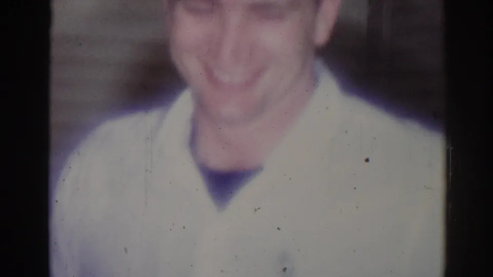 1967 home-movie frame from Los Angeles showing a smiling young man in a white martial arts gi, softly focused and close to camera.