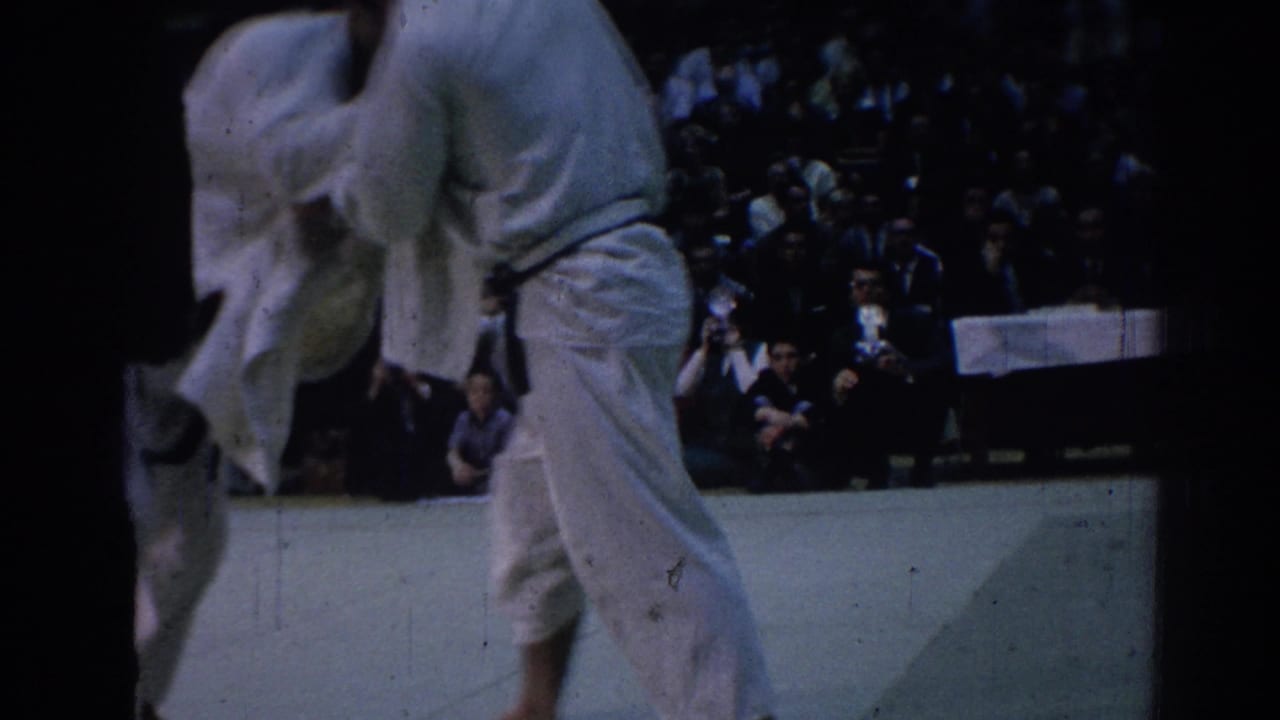 Two martial arts competitors in white gi struggle on an indoor mat before spectators in Los Angeles footage from 1967.