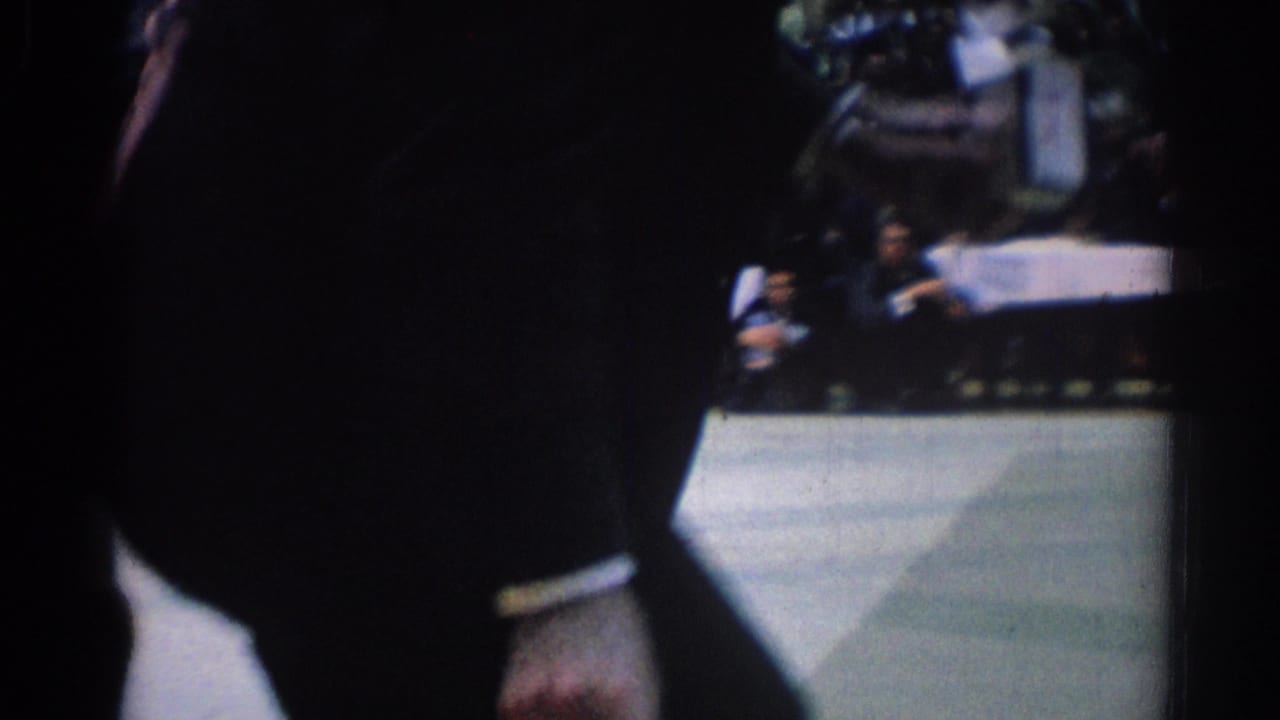 Partly obstructed view of a karate match with a fighter on a mat and spectators behind.