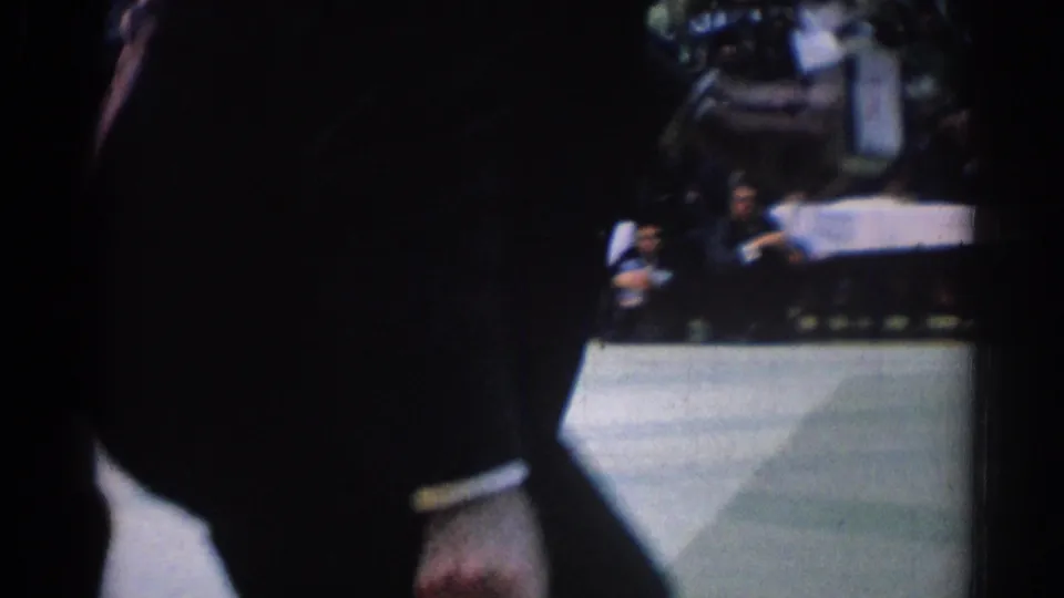 1967 Los Angeles 8mm frame showing a partly blocked spectator view of a karate competitor on a mat with an audience in back.