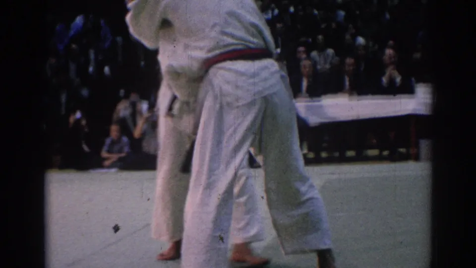 1967 Los Angeles 8mm frame showing two karate competitors in white gi meeting on a competition mat before an audience.