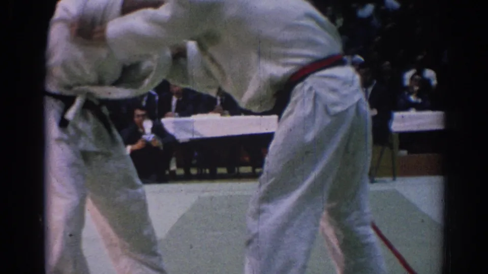 1967 Los Angeles frame showing two karate competitors in motion on a light mat, with a judging table and audience in the background.