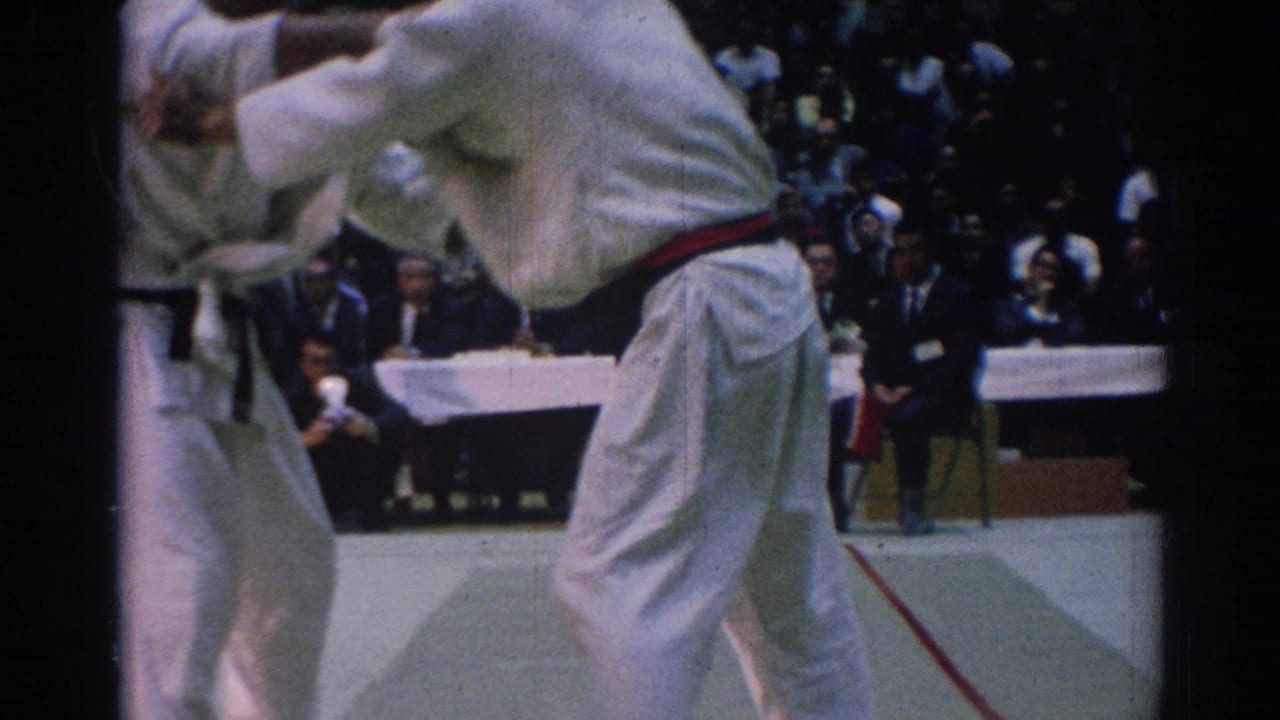 1967 Los Angeles martial arts competitors in white gi grapple near the edge of a competition mat as spectators and judges watch.