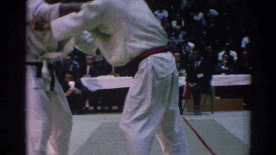 1967 Los Angeles martial arts competitors in white gi grapple near the edge of a competition mat as spectators and judges watch.