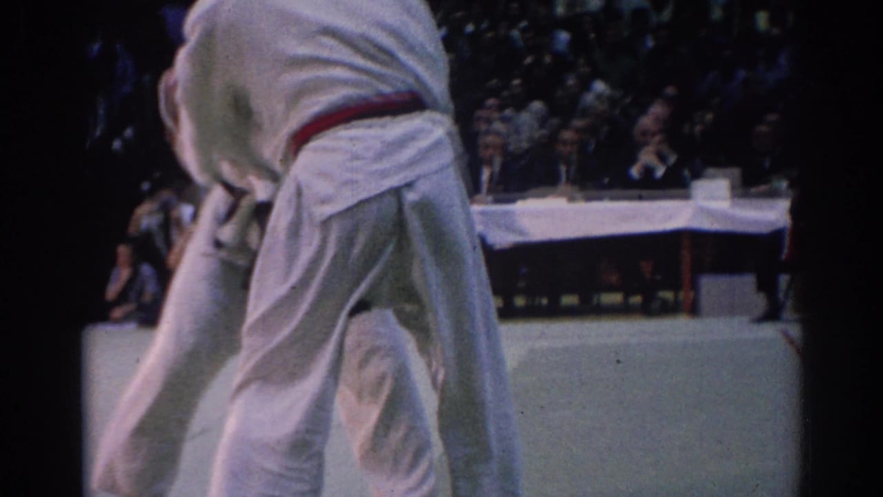 During the 1967 Los Angeles competition, a white-gi competitor leans forward on the mat with the opponent partly hidden by framing.