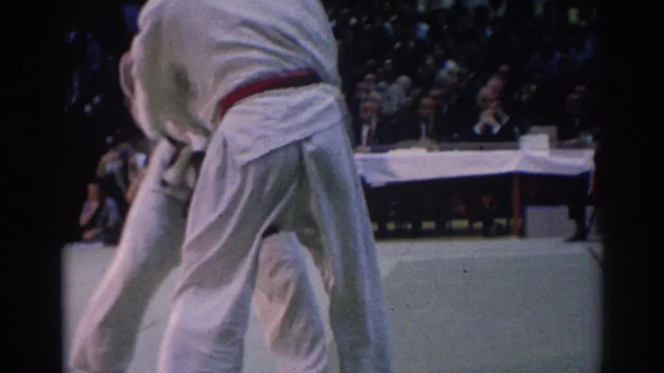 During the 1967 Los Angeles competition, a white-gi competitor leans forward on the mat with the opponent partly hidden by framing.