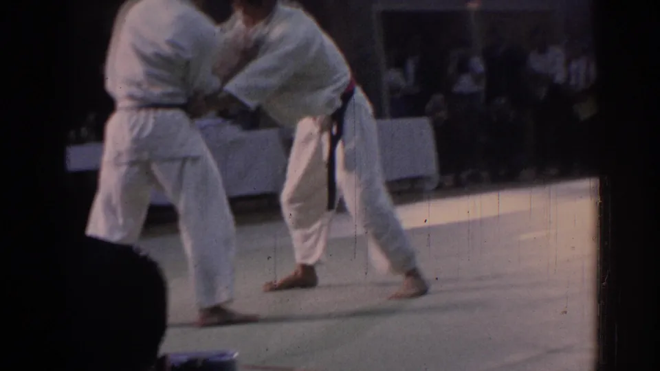 1967 Los Angeles home-movie still of a karate grappling exchange, partly obscured by a spectator or camera-side silhouette.