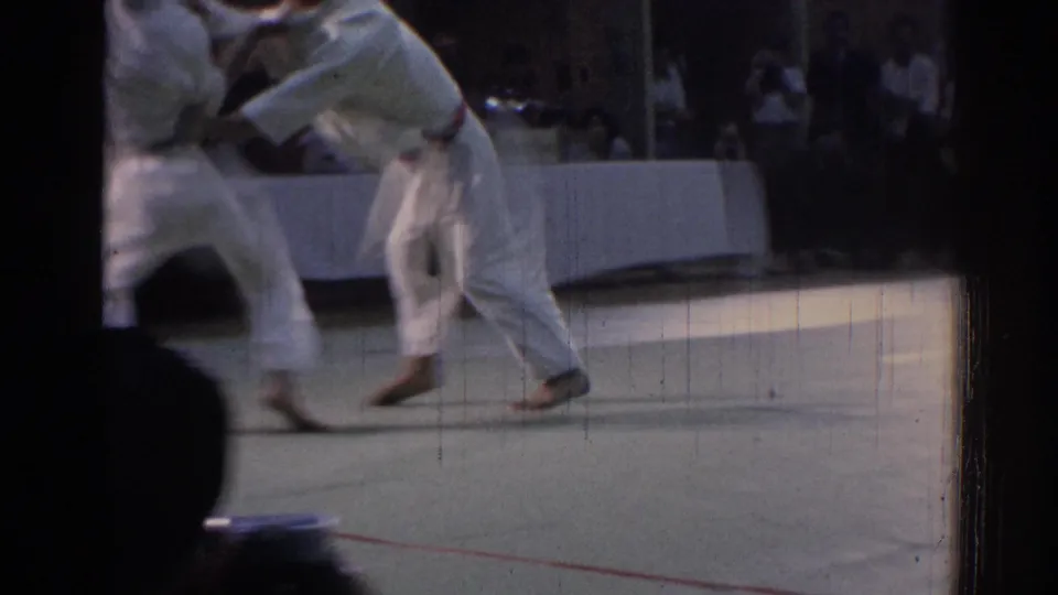 1967 Los Angeles frame showing two karate practitioners moving through a grappling exchange before a dim indoor audience.