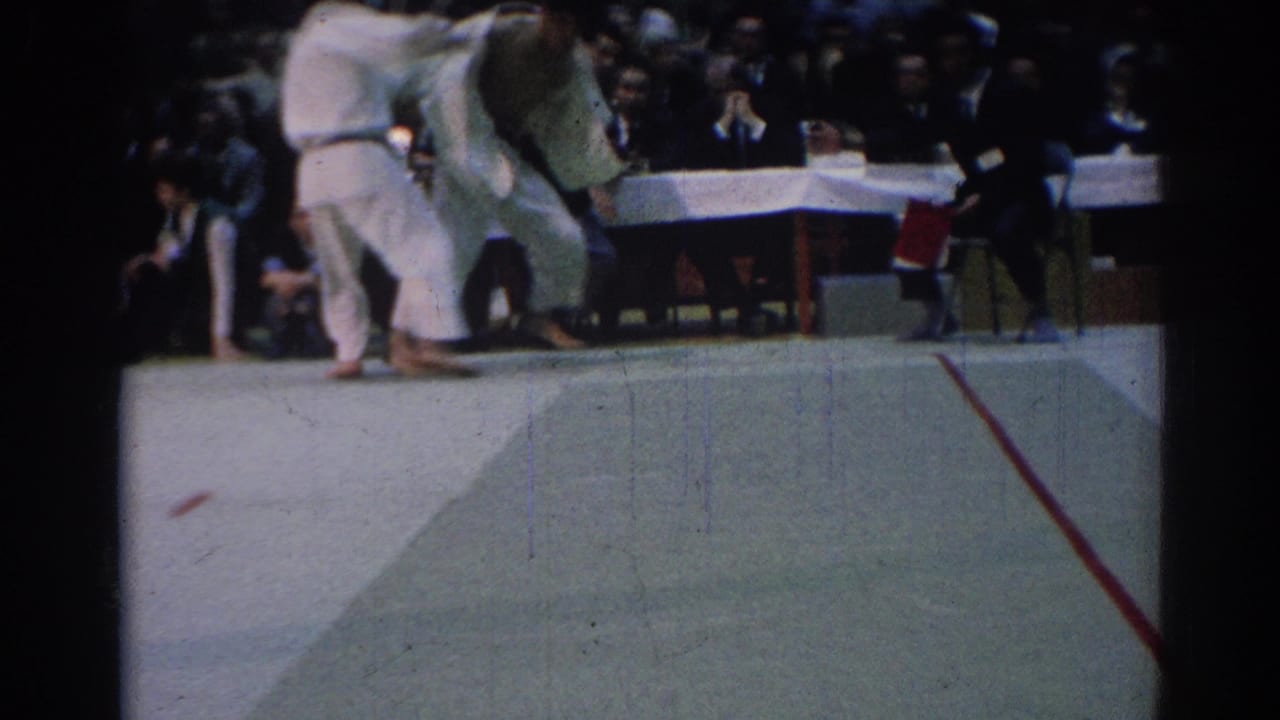A 1967 Los Angeles judo match frame shows one athlete bent low during a throwing movement while the other remains upright near the mat edge.