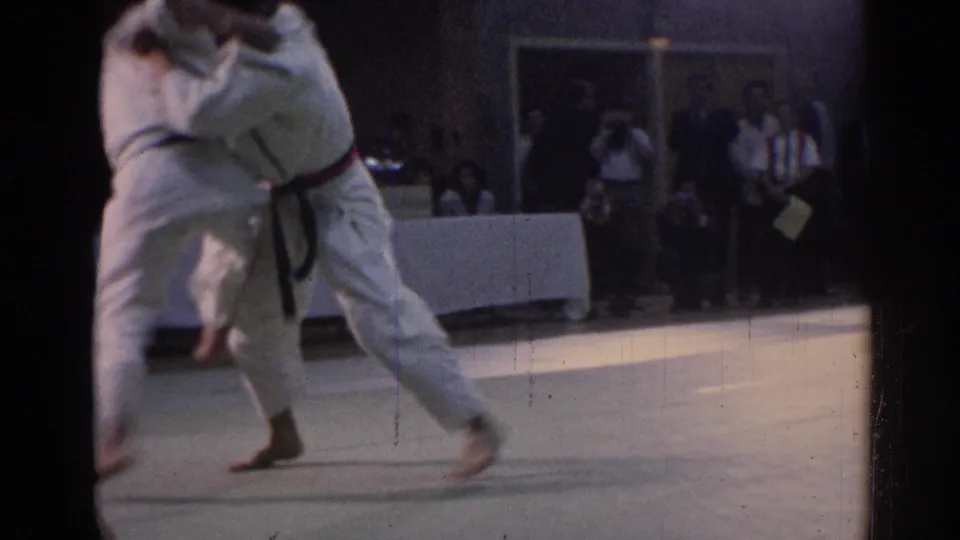 A white-uniformed competitor with a dark belt moves into a throw or takedown attempt in the indoor arena.