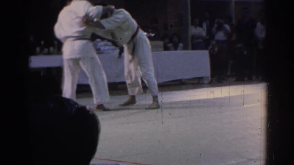 A dark-belt competitor bends forward during a grappling exchange as the opponent maintains contact in the Los Angeles match footage.