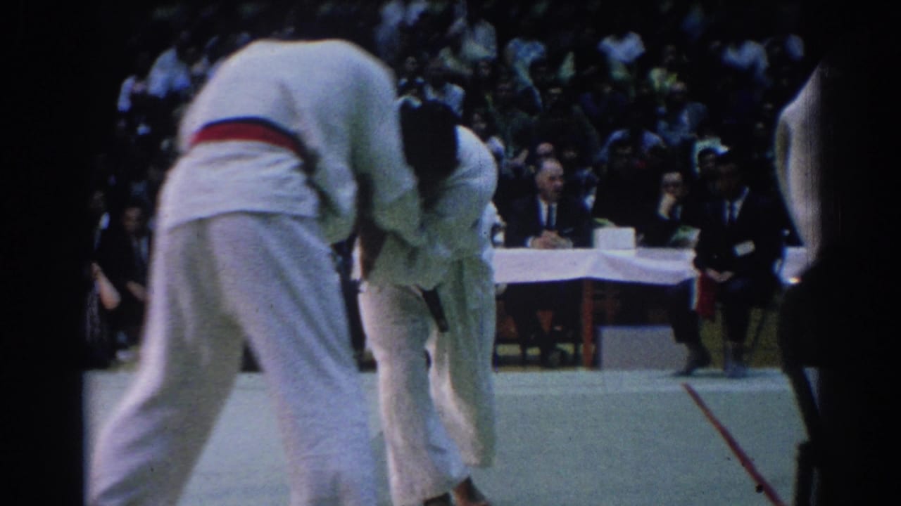 Two martial arts competitors lean into a grapple while spectators sit behind them.