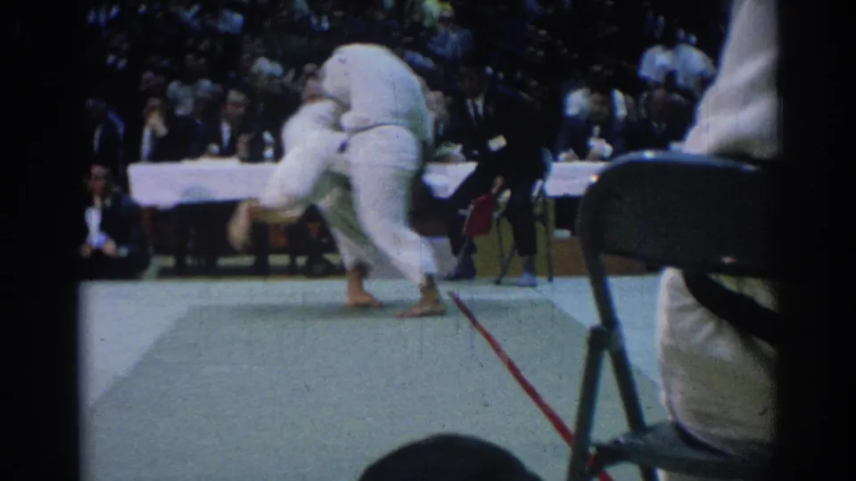 A 1967 Los Angeles indoor martial arts bout shows two competitors in white gi during a throw or takedown attempt.