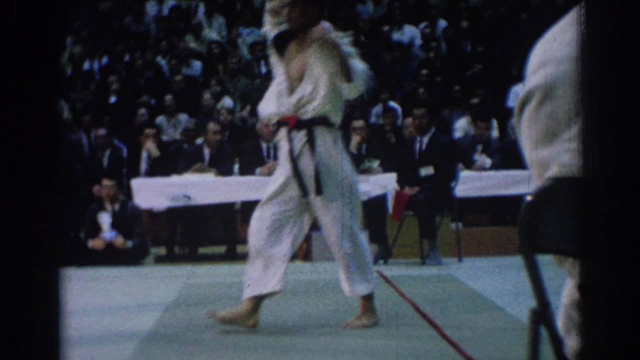 Two judo competitors in white gi stand on a mat before a crowd.