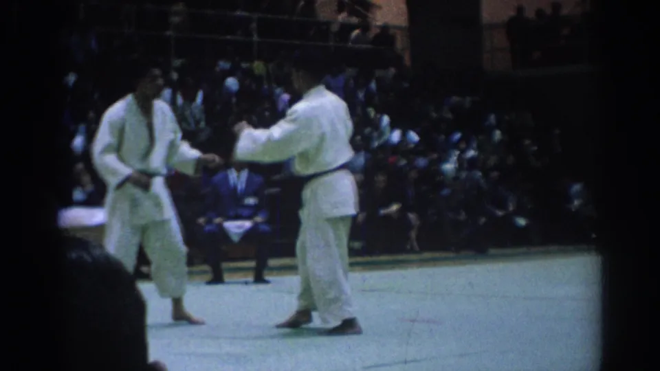 Two black-belt competitors in white gi stand at close range during a 1967 Los Angeles martial arts match.