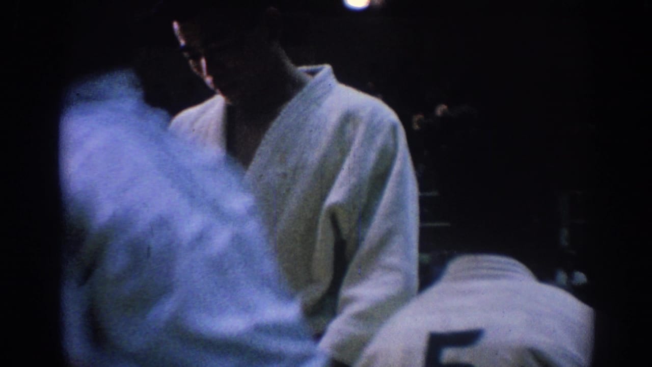 Judo competitors in white gi near the mat edge with a dark arena crowd behind them.
