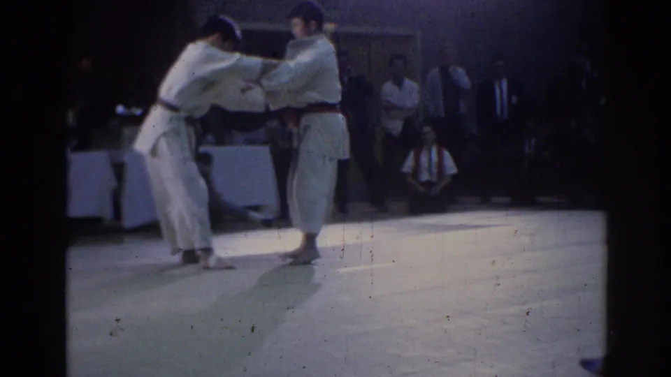 Two male judo competitors in white judogi appear to begin a grip exchange during a 1967 Los Angeles indoor match.
